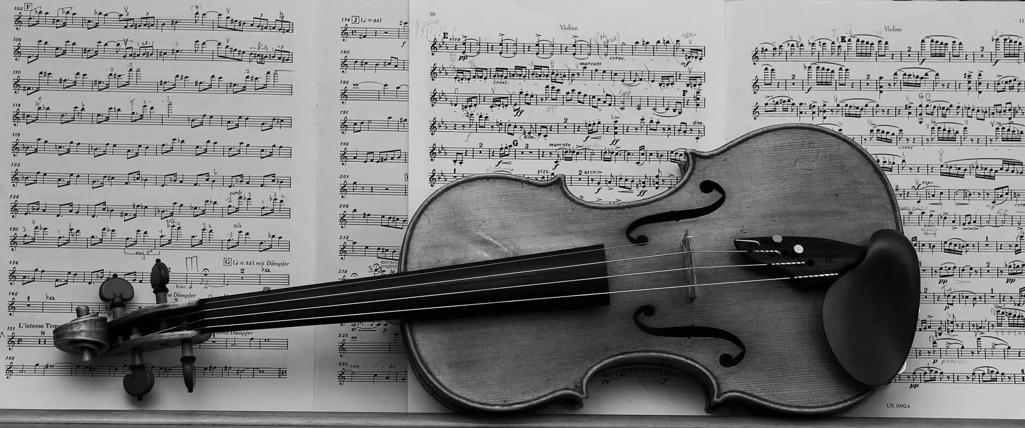A violin lies on top of open sheet music, displaying musical notes and compositions in black and white.