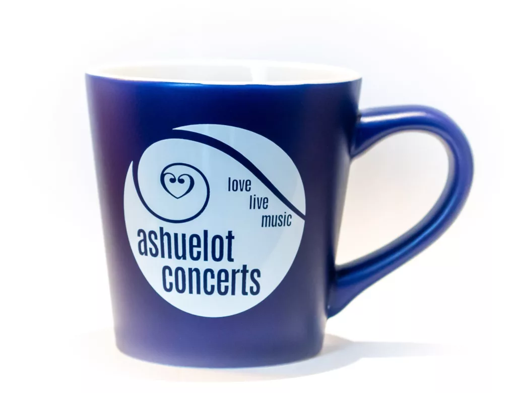 The Ashuelot Concerts Mug - Blue is a dark blue ceramic mug featuring a white circular logo with "ashuelot concerts" and "love live music" in blue text; the mug has a white interior.