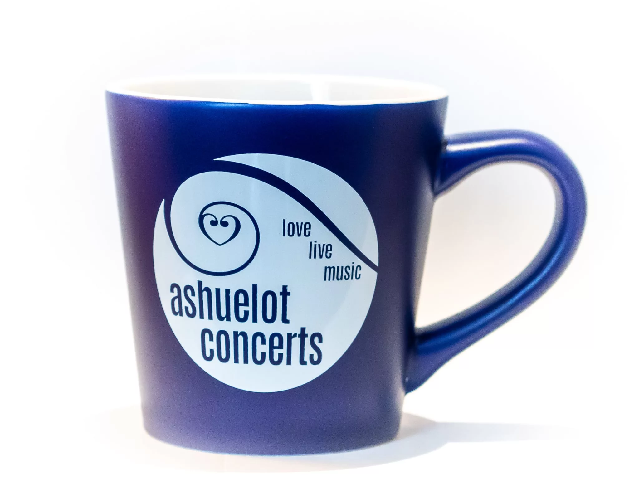 The Ashuelot Concerts Mug - Blue is a dark blue ceramic mug featuring a white circular logo with "ashuelot concerts" and "love live music" in blue text; the mug has a white interior.